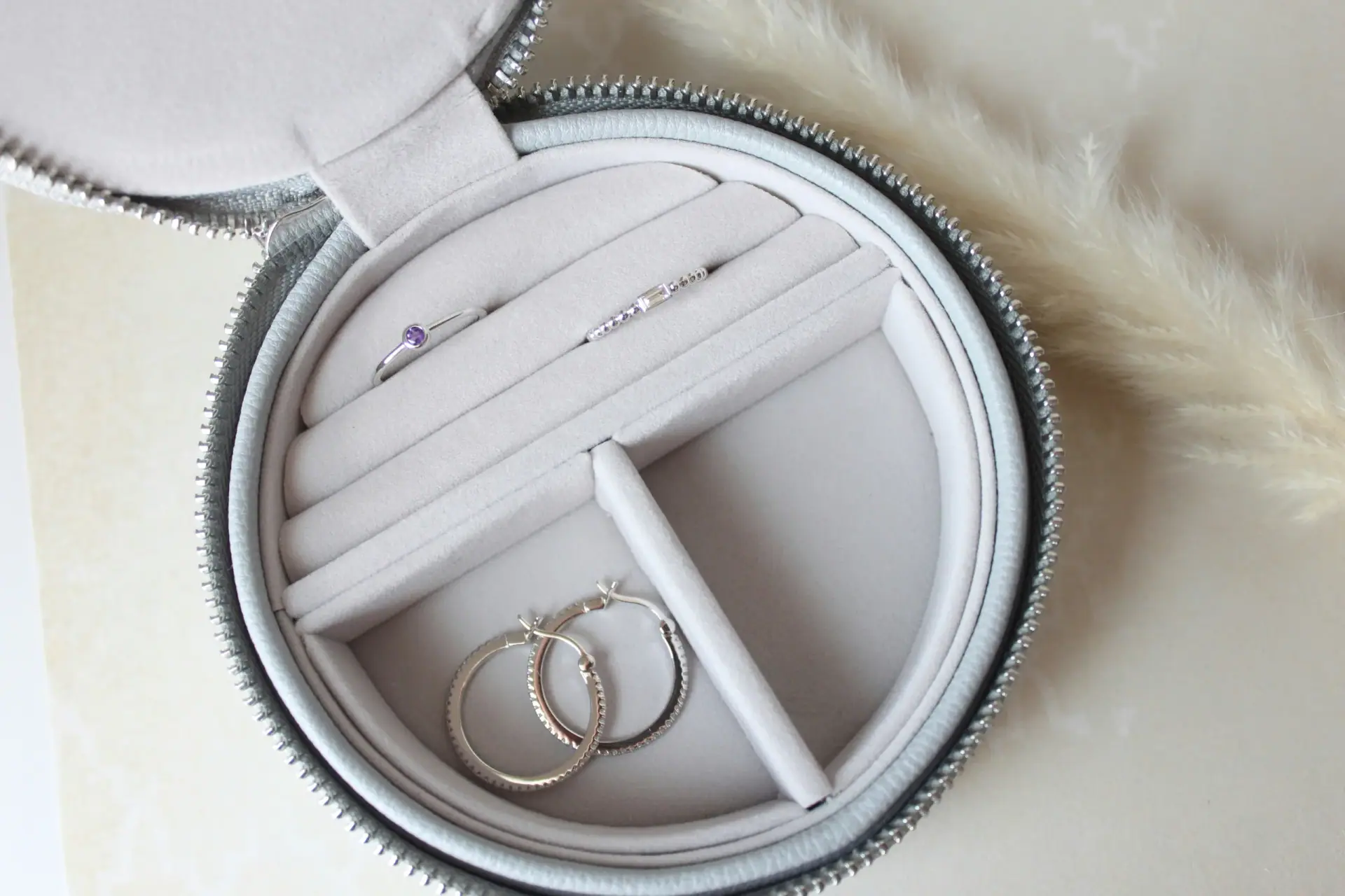 A round zip-up travel case holding rings and hoop earrings.